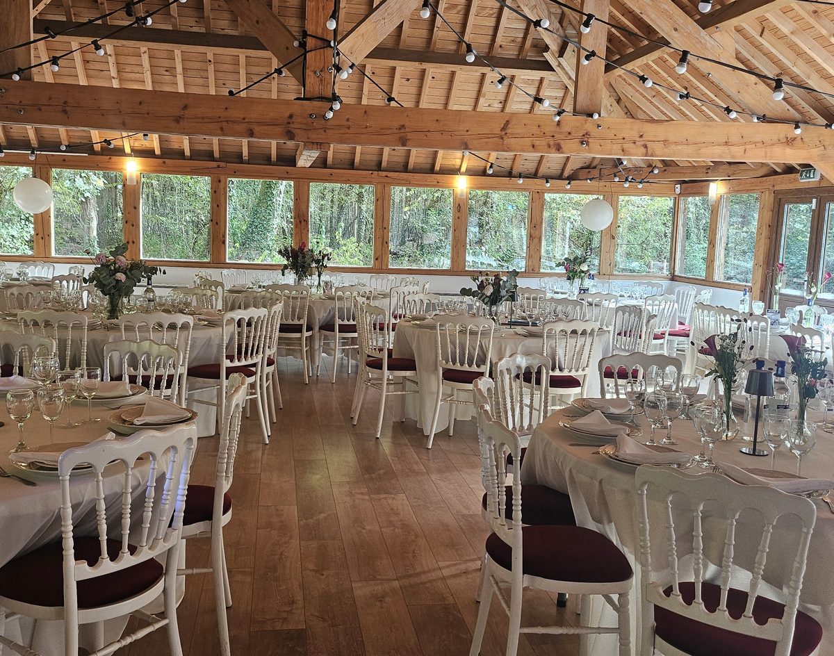 La salle dressée, tables rondes sous les guirlandes lumineuses